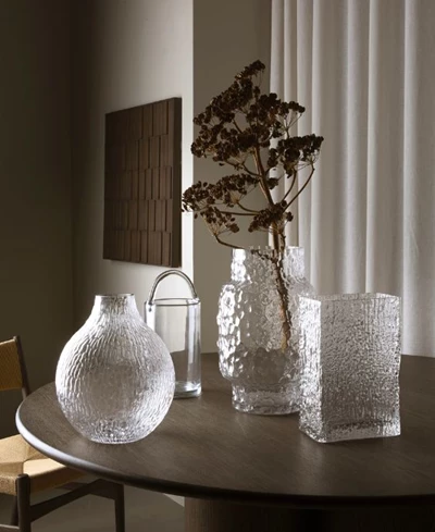 Tre genomskinliga vaser stående på ett matbord i mörkt trä.