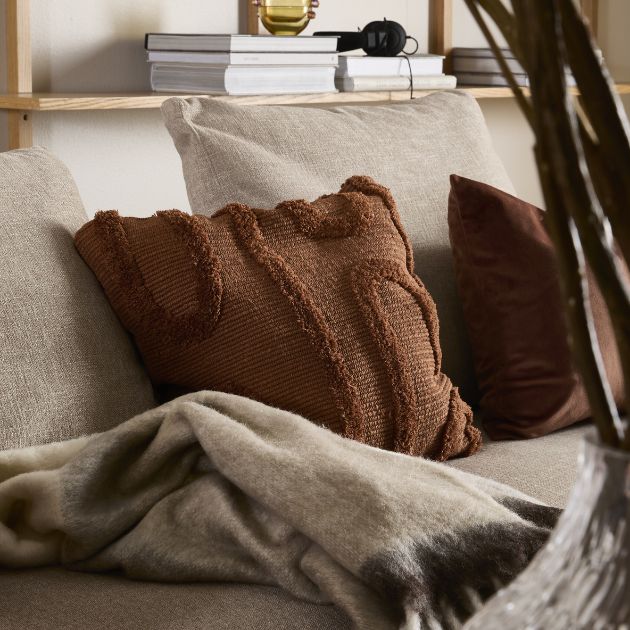 Rød pude og gråligt tæppe liggende på sofa