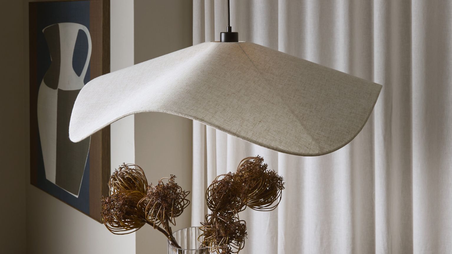 Pendellampa med böjd form hängande framför gardin.