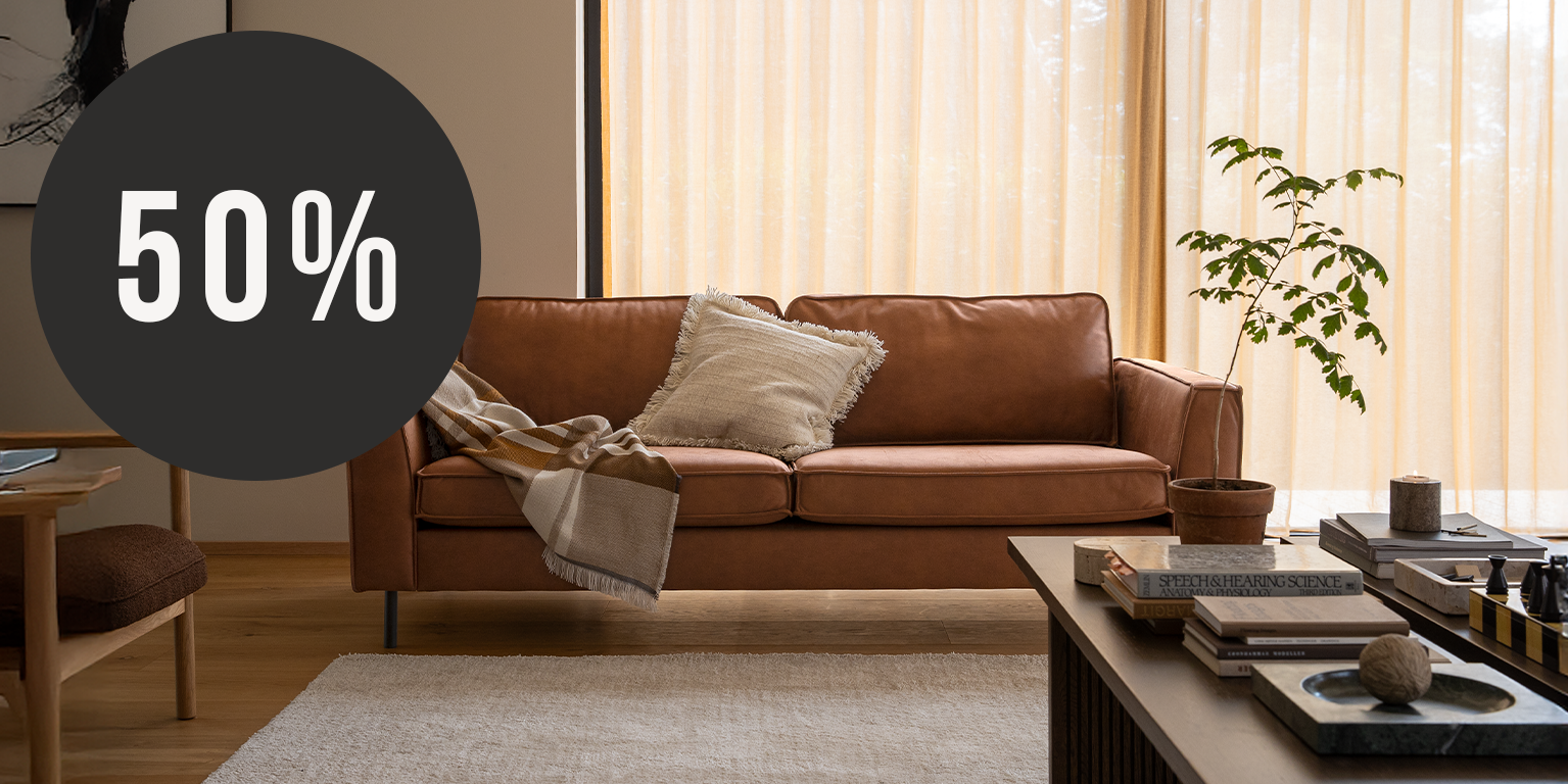 Brun lädersoffa i modernt vardagsrum med kudde och pläd, stylad med soffbord och kampanjmärke som visar 50 % rabatt