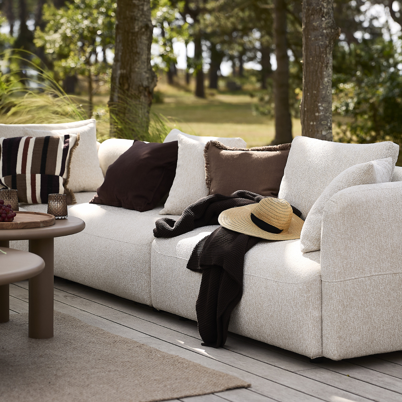 Ljus loungesoffa på terrassen med kuddar och plädar ovanpå.