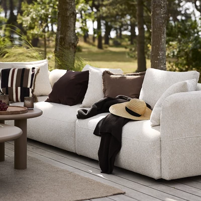 Ljus loungesoffa på terrassen med kuddar och plädar ovanpå.