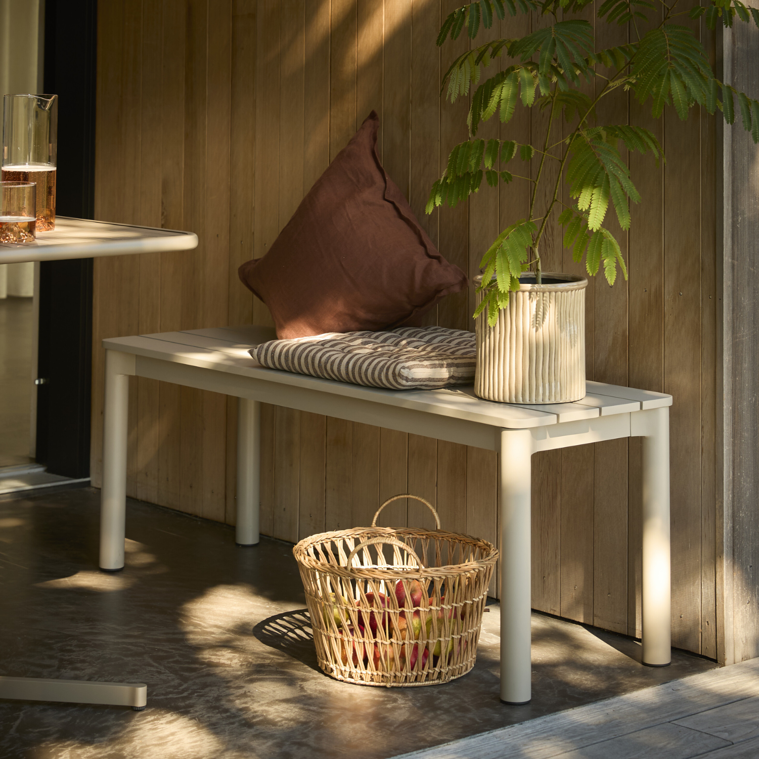 Trädgårdsbänk i grå aluminium placerad mot en vägg.