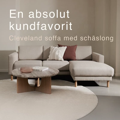 Gråaktig soffa med schäslong tillsammans med runt soffbord och rund matta.