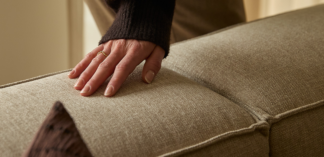 Hand som rör vid en gråaktig soffa